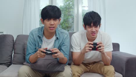 Young-Asian-gay-couple-play-games-at-home,-Teen-korean-LGBTQ-men-using-joystick-having-funny-happy-moment-together-on-sofa-in-living-room-at-house.