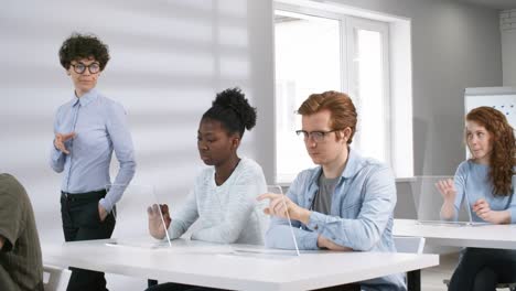 Female-Teacher-Helping-Students-Work-on-Futuristic-Touchscreen-Devices