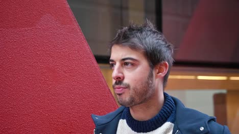 Handsome-young-man,-putting-on-wireless-earphones-while-standing-in-urban-city-background.