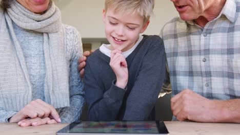 Close-Up-Of-Grandson-With-Grandparents-Playing-On-Digital-Tablet-At-Home-Together