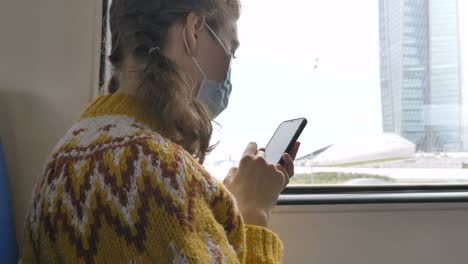 Lady-in-protective-mask-uses-phone-near-window-in-transport