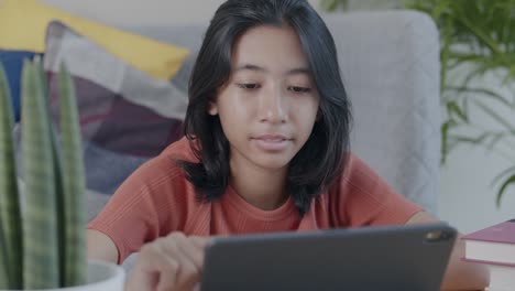 Glückliche-asiatische-Frau-mit-Tablet-im-Wohnzimmer-zu-Hause-tagsüber