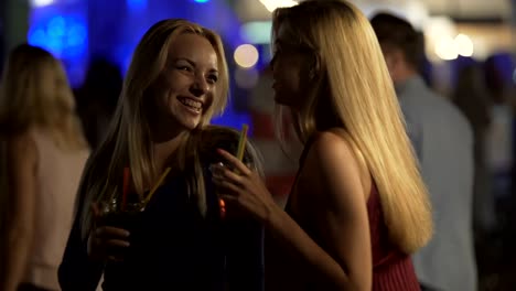 Two-sexy-blondes-flirting-with-smiles-on-pretty-faces,-dancing-at-party-in-club