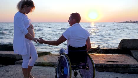 Happy-couple,-disabled-person-in-wheelchair-keeps-hand-of-pregnant-girl