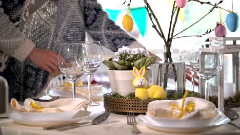 Young-woman-setting-easter-festive-table-with-bunny-and-eggs-decoration