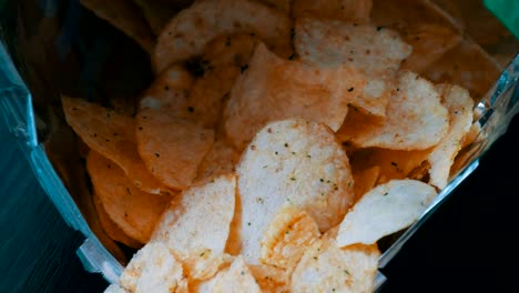 Potato-chips-in-package-on-the-table.-Female-hand-takes-chips