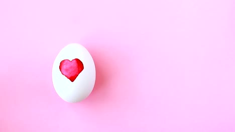 Female-hand-puts-egg-with-painted-watercolor-heart-for-Easter-on-pink-background