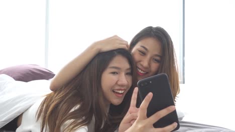 Slow-motion---Beautiful-young-asian-women-LGBT-lesbian-happy-couple-sitting-on-bed-hug-and-using-phone-taking-selfie-together-bedroom-at-home.-LGBT-lesbian-couple-together-indoors-concept.