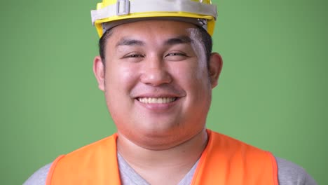 Young-handsome-overweight-Asian-man-construction-worker-against-green-background