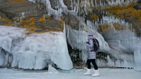 Reisen-der-Frau-auf-dem-Eis-des-Baikalsees.-Ausflug-nach-Winter-Island.-Mädchen-ist-am-Fuße-des-eisfelsen-Fuß.-Am-schönen-Eisgrotte-sucht-Reisende.-Extreme-Trek-und-zu-Fuß.-Backpacker-ruht-auf-Natur.