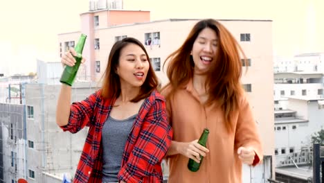 Young-asian-woman-lesbian-couple-dancing-and-clinking-bottles-of-beer-party-on-rooftop.