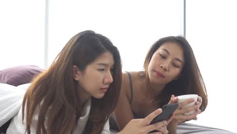 Slow-motion---Beautiful-young-asian-women-LGBT-lesbian-happy-couple-sitting-on-bed-hug-and-using-phone-together-bedroom-at-home.-Lesbian-couple-together-indoors-concept.-Spending-nice-time-at-home.