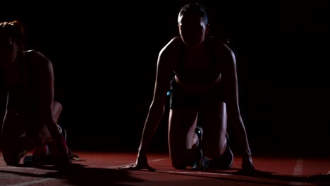 Corredores-femeninos-en-atletismo-pista-agachado-en-los-bloques-de-salida-antes-de-una-carrera.-En-cámara-lenta