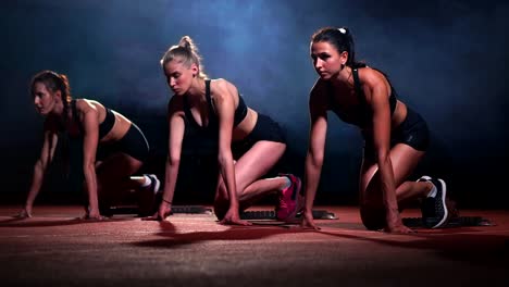 Three-sports-girls-in-black-clothes-of-the-athlete-at-night-on-the-treadmill-will-start-for-the-race-at-the-sprint-distance-from-the-sitting-position