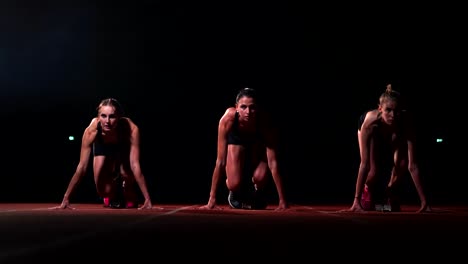 Tres-chicas-en-ropa-de-color-negro-están-en-las-almohadillas-de-partida-para-iniciar-la-carrera-en-la-competencia-a-la-luz-de-las-linternas