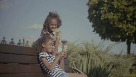 Cheerful-kids-with-smart-phone-sitting-on-bench