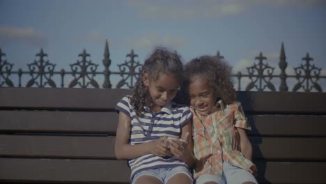 Kids-chatting-online-using-smart-phone-on-bench