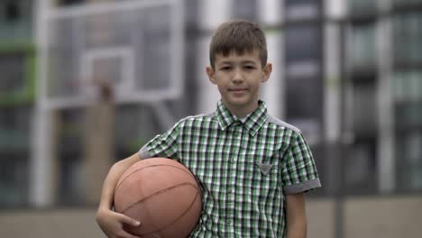 Retrato-de-un-niño-con-una-pelota-de-baloncesto-en-una-cancha-de-baloncesto,-mira-a-la-cámara