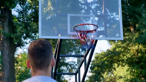 La-parte-trasera-del-hombre-saltando-y-lanzando-baloncesto,-bola-golpea-anillo,-pasando-por-el-aro,-jugando-en-el-parque,-durante-el-día