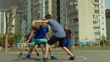 Teenage-streetball-player-dribbling-and-bouncing-the-ball-on-the-floor,-passing-to-his-teammate-while-playing-basketball-game-on-street.-Basketball-guard-stealing-a-ball-and-running-in-fast-break.