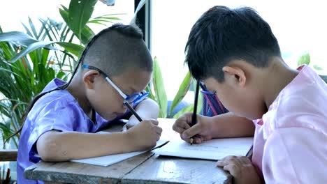 Happy-little-asian-boy-with-writing-in-notebook-and-pencils-drawing-at-home.-education-concept