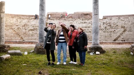 Happy-senior-man-and-women-with-young-girl-waving-on-video-chat-with-family-near-old-amphitheater-ruins-in-Ostia,-Italy.