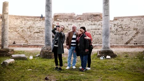 Smiling-senior-family-and-young-woman-tourists-waving-on-video-call-to-family-at-old-amphitheater-ruins-in-Ostia,-Italy.