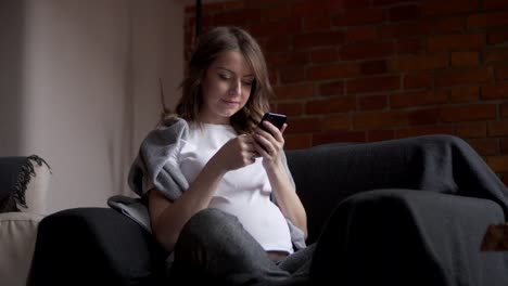 Pregnant-woman-using-mobile-phone-on-arm-chair