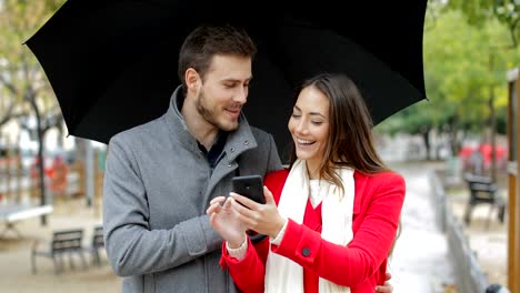 Happy-couple-checking-smart-phone-under-the-rain