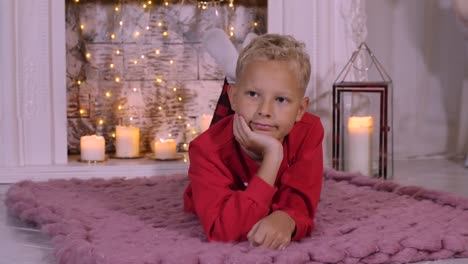 Portrait-teenager-boy-lying-on-cozy-carpet-on-Christmas-fireplace-background