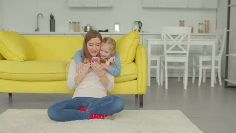 Hija-viendo-dibujos-animados-en-el-teléfono-y-mamá-alegre