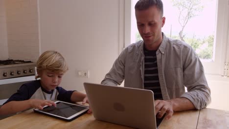 Padre-e-hijo-usando-computadoras-en-la-mesa-de-la-cocina,-filmado-en-R3D