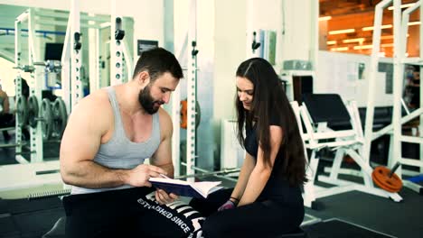 Trainer-helps-young-strong-brunette-woman-write-training-program-in-fitness-club-and-gym-center