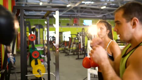 Young-woman-boxer-hit-punching-bag-during-pre-match-warm-up-with-her-trainer-in-boxing-club