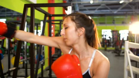 Young-woman-boxer-hit-punching-bag-during-pre-match-warm-up-with-her-trainer-in-boxing-club