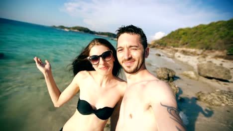 Joven-pareja-feliz-hablando-con-amigos-a-través-de-Internet-utilizando-el-teléfono-inteligente-en-la-playa-oceánica