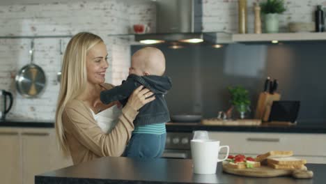 Juegos-de-joven-madre-con-su-bebé-hermoso-mientras-de-pie-en-la-cocina.-En-cámara-lenta.