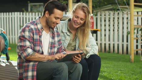 Hombre-joven-y-mujer-usando-la-pantalla-táctil-de-la-tableta-ordenador-juntos,-que-están-en-el-patio-trasero-en-el-día-de-verano-brillante.