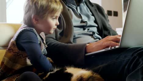 moderne-Familie-kleines-Mädchen-spielt-mit-Katze-während-Papa-arbeitet-mit-Notebook-auf-Couch-indoor-in-modernen-industriellen-Haus.-Kaukasische.-4k-handheld-nahaufnahme-Slow-Motion-video-gedreht