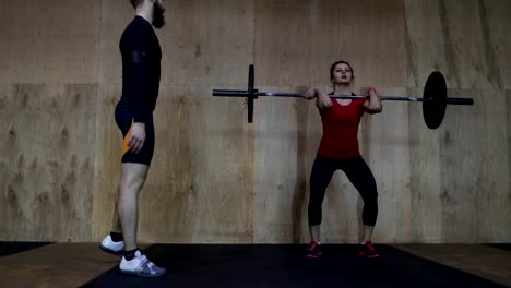 Sportliche-Frau-Heben-von-Gewichten-mit-Personal-Trainer-im-Fitness-Studio-trainieren