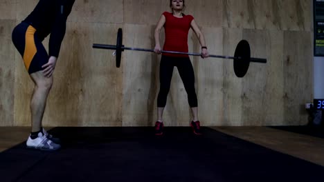 Sportliche-Frau-Heben-von-Gewichten-mit-Personal-Trainer-im-Fitness-Studio-trainieren