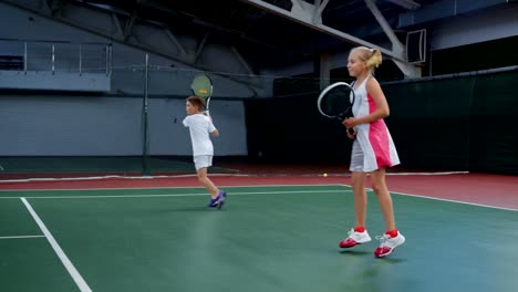 Deportivo-niño-y-niña-practicando-con-raquetas-de-tenis-en-cancha-de