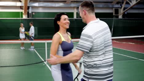 Zwei-männliche-und-weibliche-Tennis-Team-Lächeln-und-Händeschütteln-auf-Platz