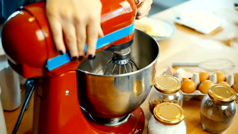 Vista-de-primer-plano-de-mujer-joven-preparando-la-masa-en-el-recipiente.-Mujer-enciende-la-batidora-para-mezclar-los-ingredientes