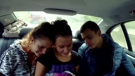 Tres-adolescentes-miran-red-social-smartphone-de-conducción-en-la-parte-trasera-de-coche-de-lujo