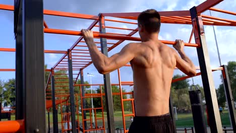 Back-side-view-of-young-topless-sportsman-chin-ups.-Sports-field-in-background.