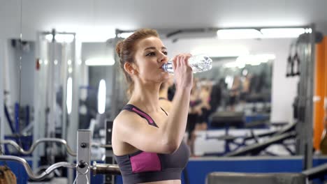 Deportes-niña-bebidas-agua-de-una-botella-de-plástico-en-el-gimnasio-entre-los-ejercicios-60-fps