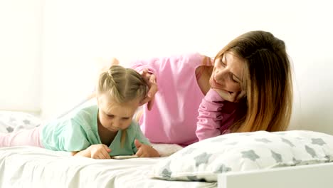 Feliz-joven-madre-e-hija-jugando,-dibujo,-juegos-en-el-teléfono-inteligente-trenza-trenzas,-leer.