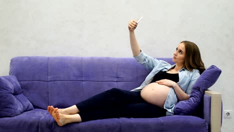 Beautiful-pregnant-woman-sitting-on-sofa-in-living-room-Dalet-selfie-for-social-networks