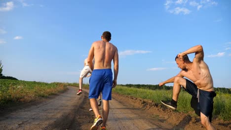 Männliche-Freunde-gehen-auf-Landstraße-und-Spaß-haben.-Gruppe-von-glücklichen-jungen-Narren-um-im-Freien.-Rückansicht-Rückansicht-niedrigen-Winkel-hautnah